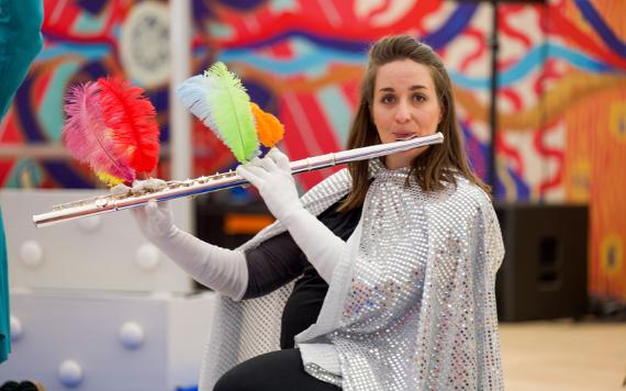 Woman in a sparkly cape plays a flute