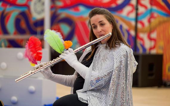 Woman in a sparkly cape plays a flute