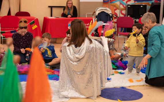 Woman in a sparkly cape plays a flute to children