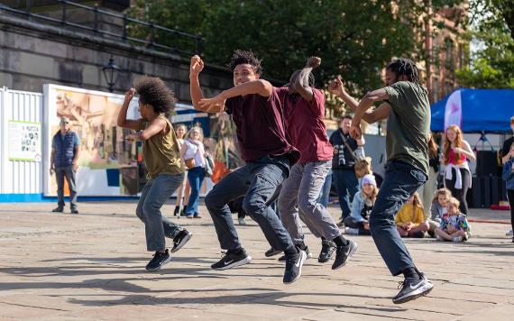 A performance group jumping in the air mid dance in front of a crowd