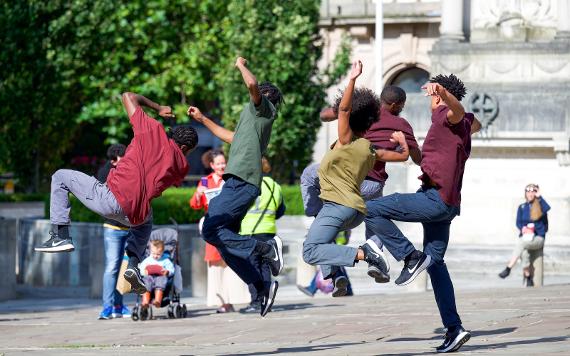 A performance group hopping in the air in front of a small audience