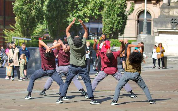 A performance group look up to the sky mid dance in front of a crowd