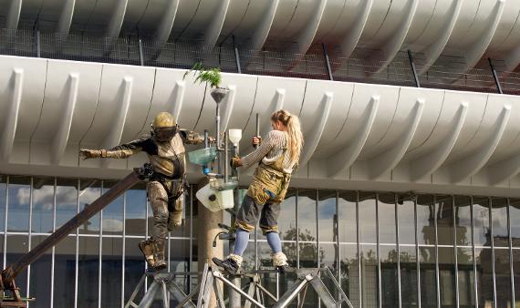 An astronaut and a woman balance on a metal frame