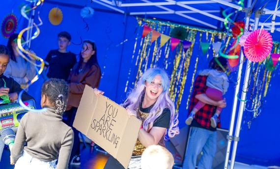 A woman under strings of bunting holds a sign up that says You Are Sparkling