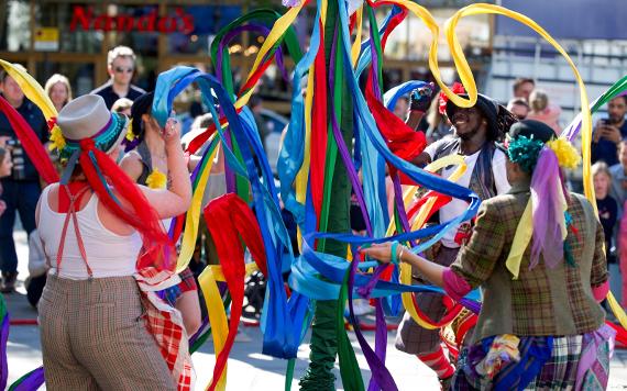 A dance group play with multi coloured ribbons around a maypole