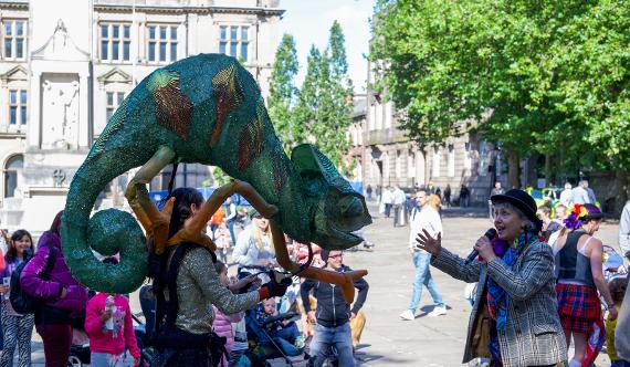 A woman with a microphone greets an animatronic chameleon