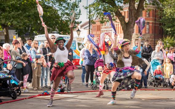 Three women dancing energetically with colourful ribbons in front of a crowd