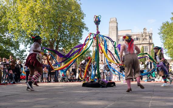 The Step Hop House group dances around a maypole with colourful ribbons and colourful hats