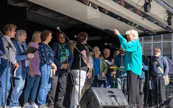 The Preston People's Choir performing on a stage as a conductor directs them