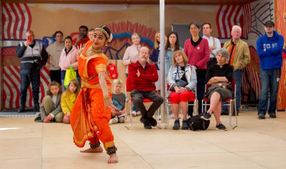 A lady from the Swati Dance Company wearing a bright orange sari dances to an audience