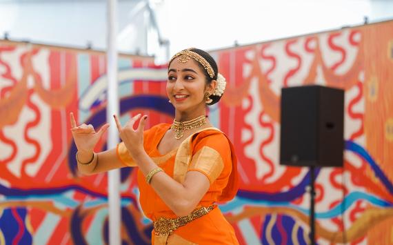 A dancer in an orange sari performing graceful hand movements in a dance routine