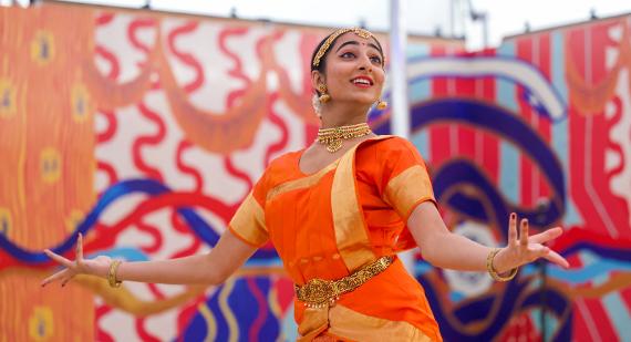 A dancer in an orange sari looks up smiling while dancing for the Swati Dance Company