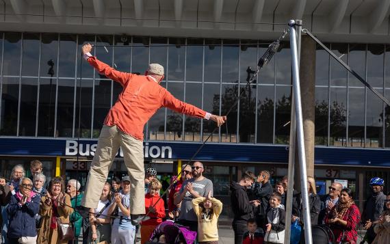 A man in a red shirt balances himself on a tight rope in front of an audience