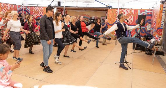 A group of people follow a man leading a swing dance routine on a dance floor