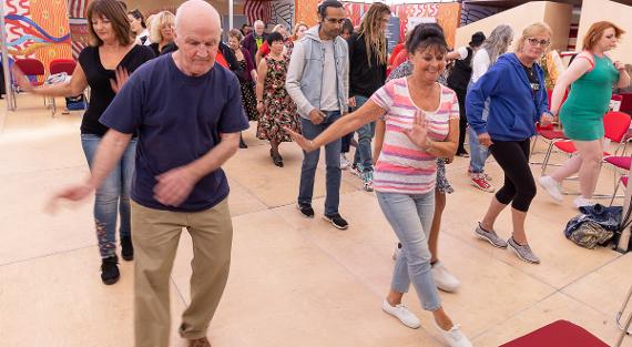 A group of men and women young and old swing dancing on a dance floor