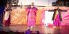 A Jatra performance on a stage at Preston Markets with performers wearing bright purple clothes and singing