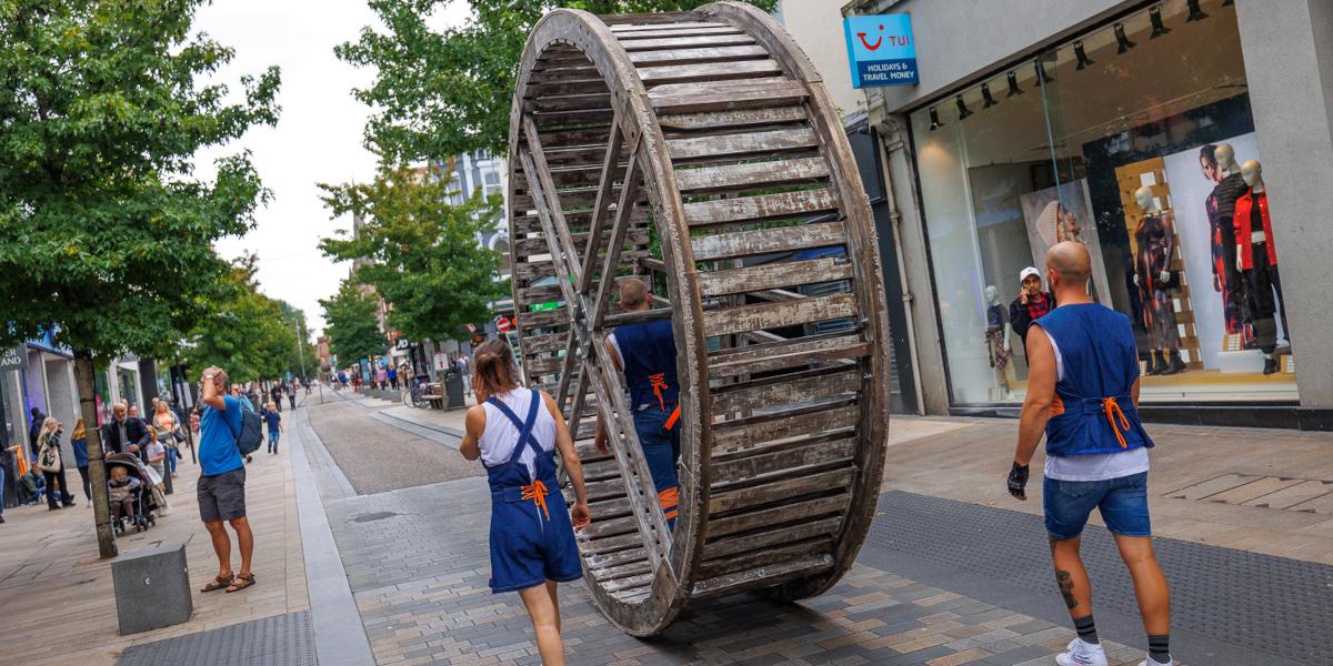 Performers roll a large wooden wheel down Fishergate Street in Preston