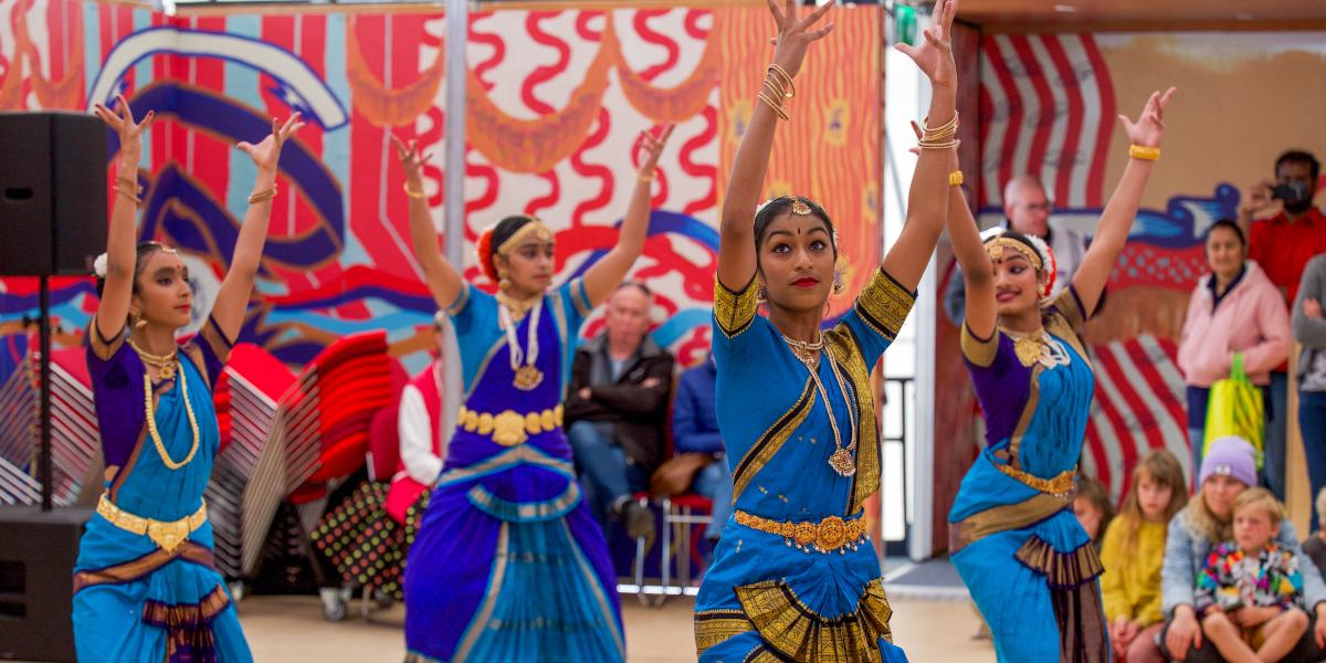 A group of dancers from the Swati Dance Company in blue dresses perform a dance routine in the Mobile Event Tent