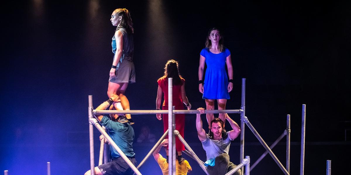 Performers from WILD posing on scaffolding during their routine on stage