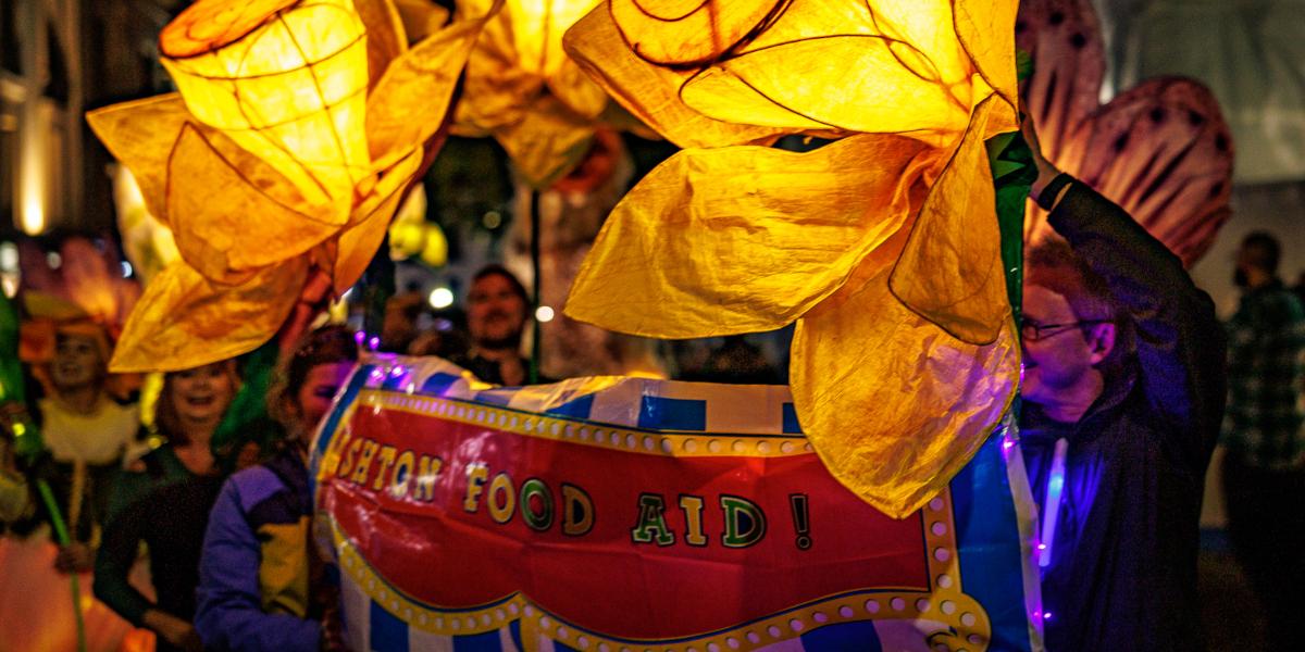 A procession of people carrying a banner with large yellow flowers for Encounter Festival 2023