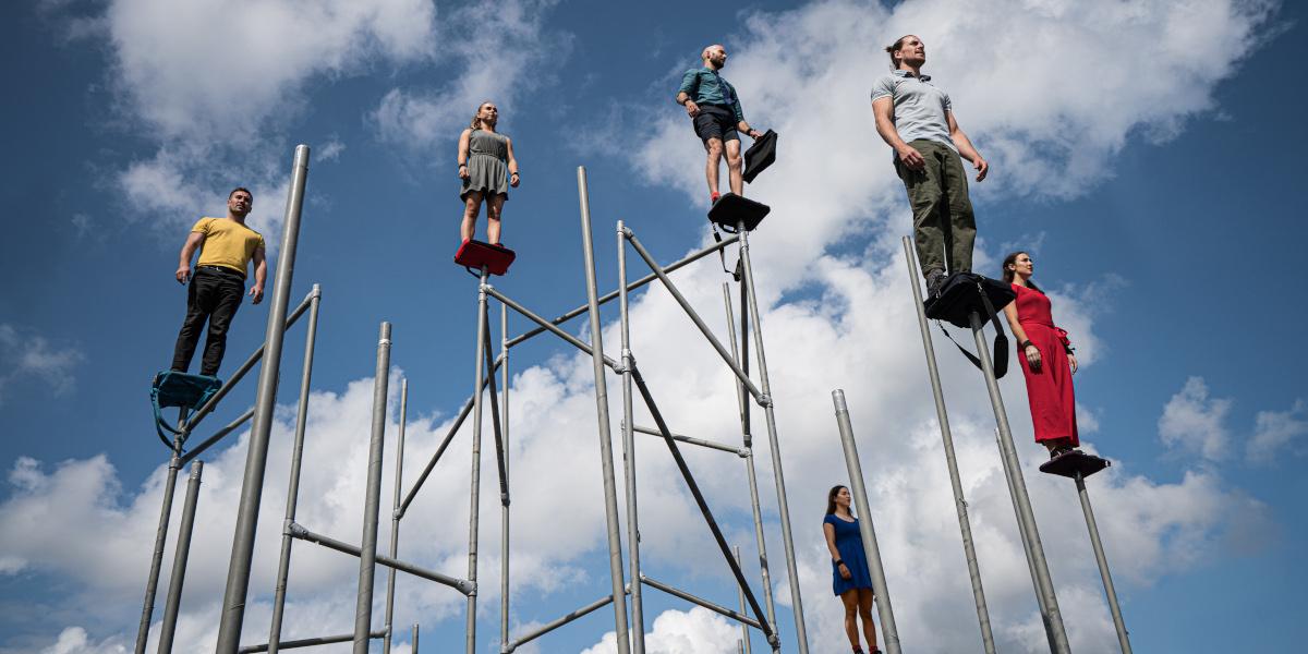 A group of WILD performers stand high in the air on metal pipes