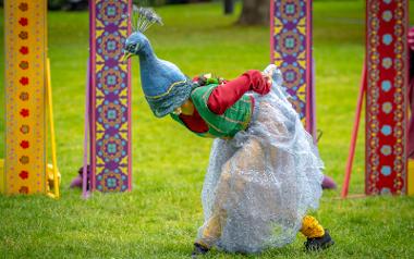 A performer wearing a dress and a hat shaped like a peacock mid dance