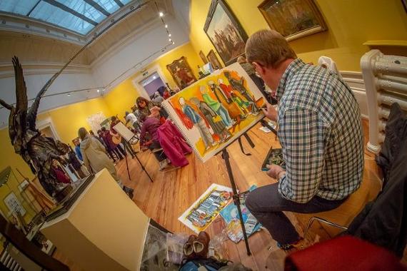 Gathering of artists and spectators inside the Harris art gallery, with one man painting the crowds.