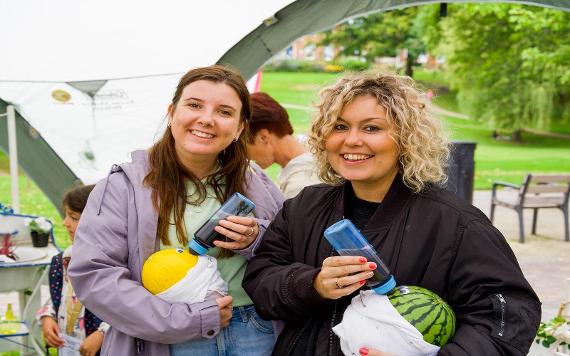 Two ladies feeding a melon with a baby bottle